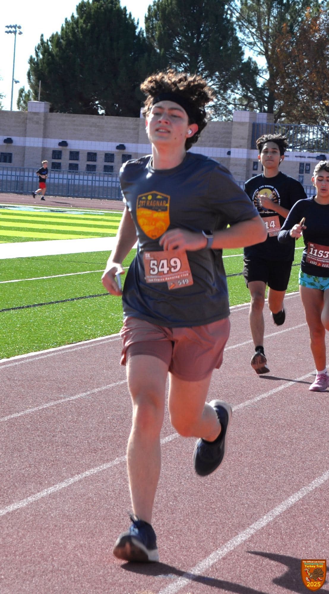 Cruce running on a track in a headband and race bib 549, other runners behind him.